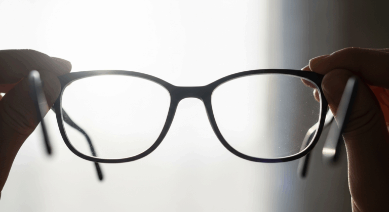 A person holding up a pair of spotlessly clean eyeglasses to the light, showing off the sparkling, clear lenses.